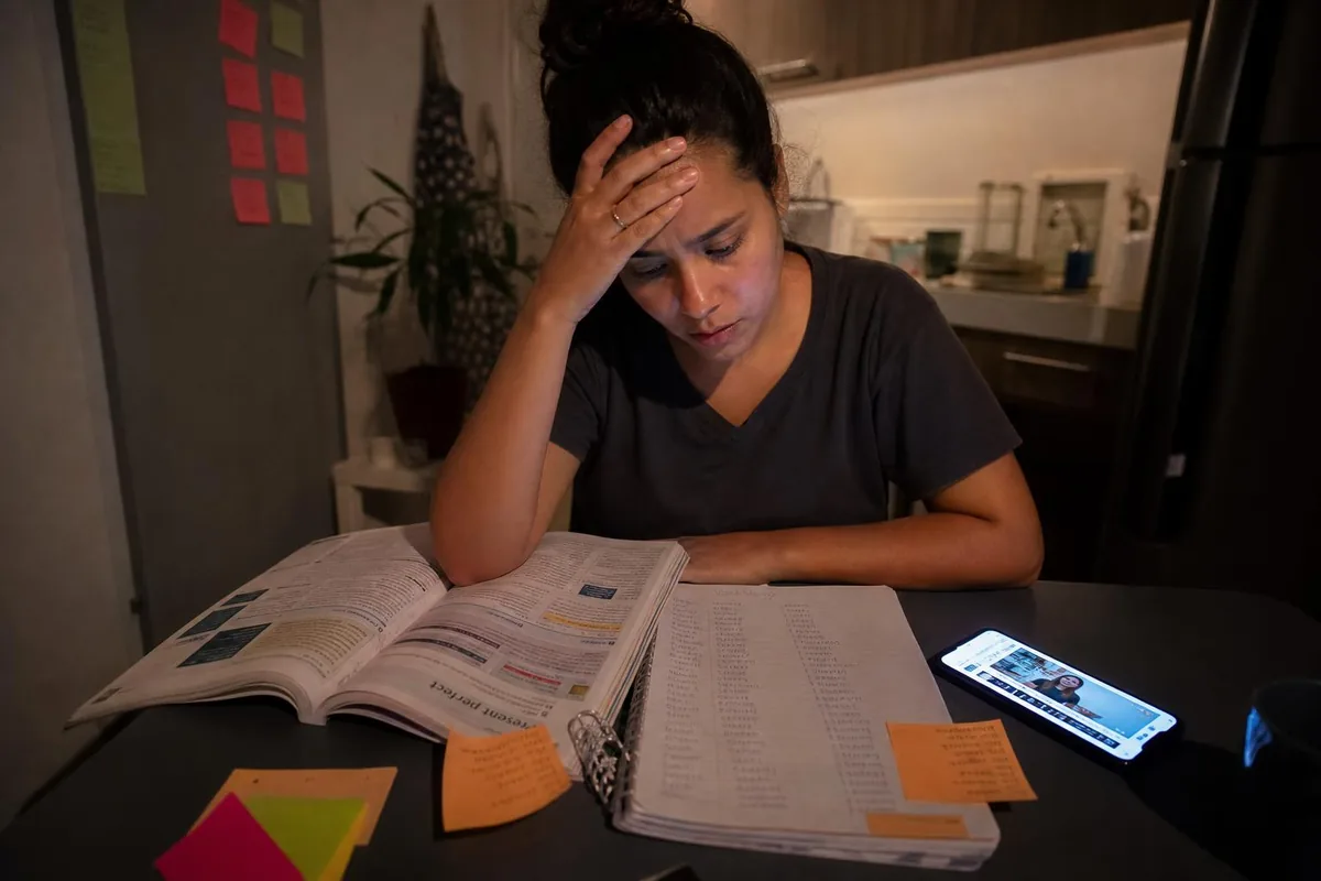 Mulher cansada estudando inglês à noite com livro de gramática e listas de palavras